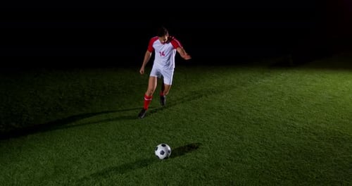 Soccer Player Kicking Ball on Field at Night