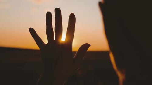 Mädchen schaut bei Sonnenuntergang durch ihre Hand auf die Sonne