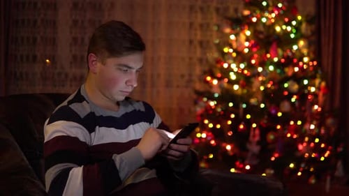 Young Adult Using Phone By Christmas Tree