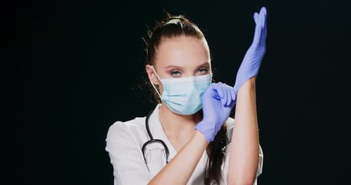 Woman Doctor Puts on Gloves, Wearing Face Mask