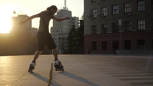 Young Long-haired Man Is Professionally Skating Between Cones on a Nice Evening Sunset in a City