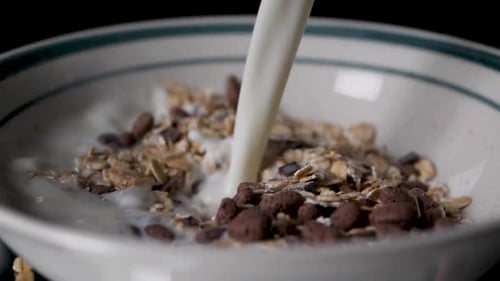 Filing milk on cereals, which are in a white bowl with a green circle on it in slow motion.
