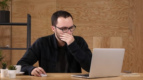 Frustrierter Geschäftsmann, der seinen Kopf hält, sitzt im Büro.