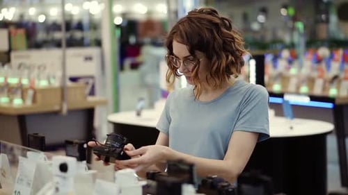 Young Curly Woman in Glasses Shopping for a New Photocamera in the Electronics Store