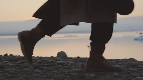 Person Walks Along Rocky Beach at Dusk