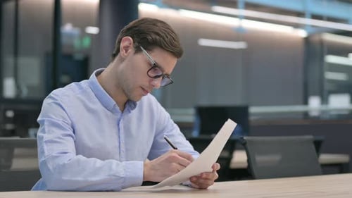 Young Adult Man Writing at Desk in Modern Office