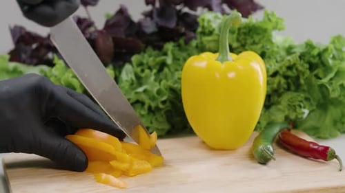 Gloved Hand Cuts Yellow Pepper on Cutting Board
