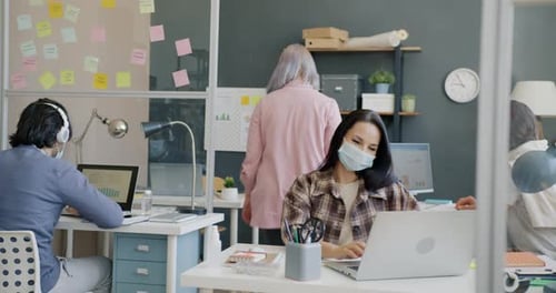 Young Woman Wearing Face Mask Doing Elbow Bump with Colleague and Working with Computer in Office