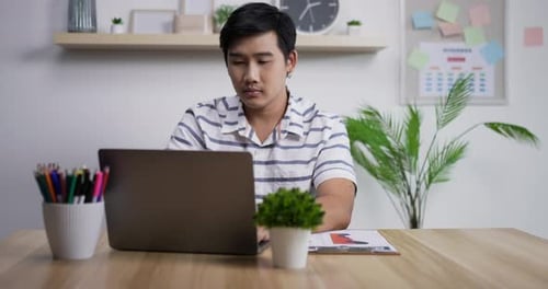 Thoughtful Asian businessman working on laptop computer in home office
