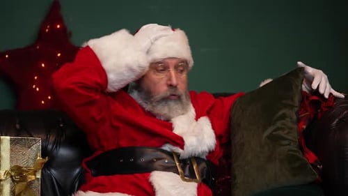Le père Noël fatigué dort sur le canapé, se réveille, vérifie si les cadeaux sont sur place et s'endort