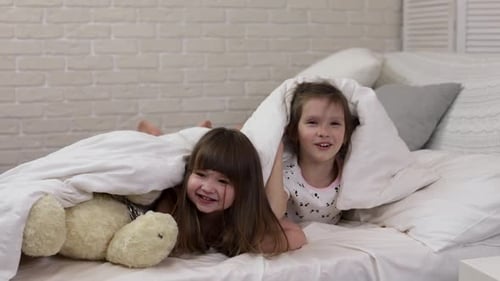 Playful Girls Building Fort on Bed with Teddy Bear