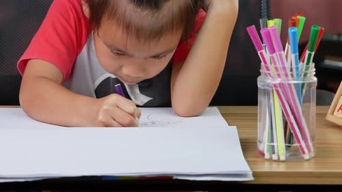 Una linda niña dibuja un arcoíris y un árbol con lápices de colores en la mesa de su casa.