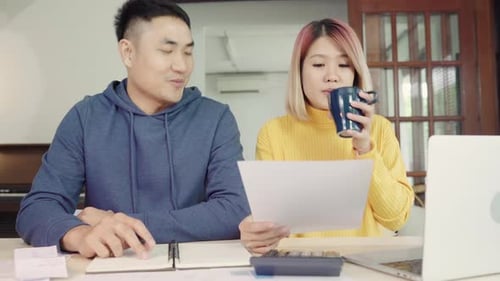 Young couple managing finances, reviewing their bank accounts using laptop and calculator at home