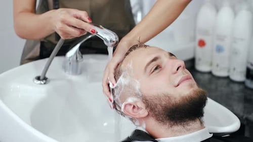 Hair Stylist Washing Young Man's Hair in Salon
