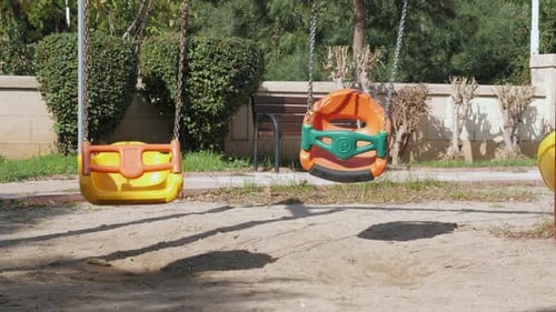 Empty swing seats swaying on children playground.