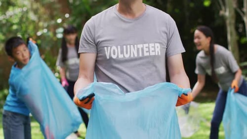 Smiling asian man wearing volunteer t shirt holding refuse sack for collecting plastic waste
