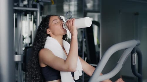 Woman Drinks Water After Gym Workout on Elliptical
