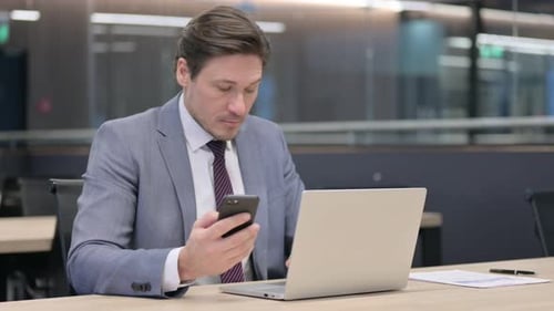 Middle Aged Businessman working on Laptop and Smartphone in Office
