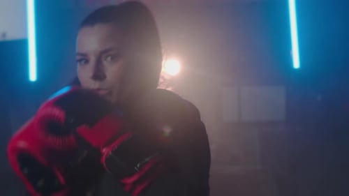 Close-up Point of view of a young brunette woman punches and kicks, looking into camera.