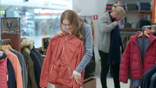 Charming Young Woman Examining Coat in Clothing Shop and Smiling at Camera. Portrait of Confident
