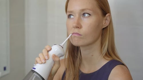Eine junge Frau benutzt eine tragbare Munddusche mit Wasserzahnseide, um ihre Zähne zu reinigen. Zahnpflege