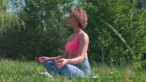 Attractive slim woman meditates and practices yoga in a public park