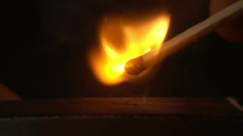 Match Igniting into Bright Orange Flame in Darkness