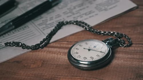 Antique Stopwatch Lies on Wooden Desk with Old Documents and Counts Seconds