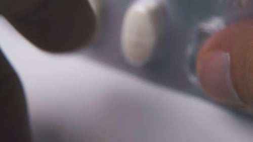 Hands Pushing Pill out of Packaging Close Up