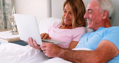 Smiling Senior Couple Using Laptop in Bed