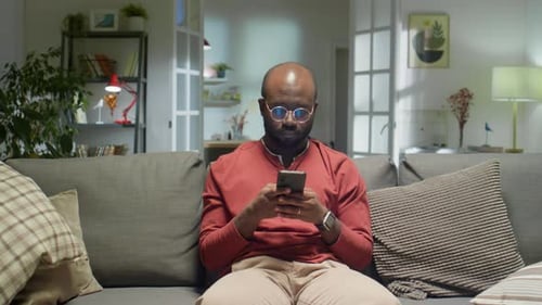 African American Man Sitting on Sofa and Typing on Phone