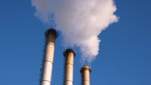 Industrial Smokestacks Emitting Plumes of Smoke Against Blue Sky