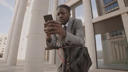 Young Adult Using Phone on Electric Scooter in City
