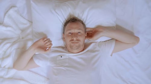 Man Lying in Bed Stretches and Smiles