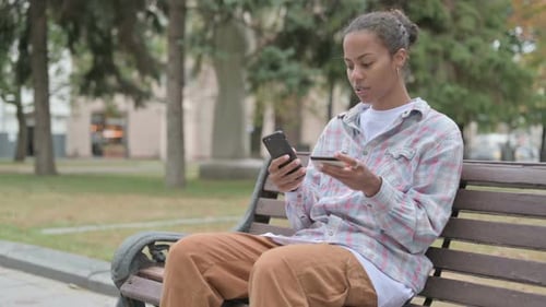 African Woman Shopping Online on Smartphone While Sitting Outdoor on Bench