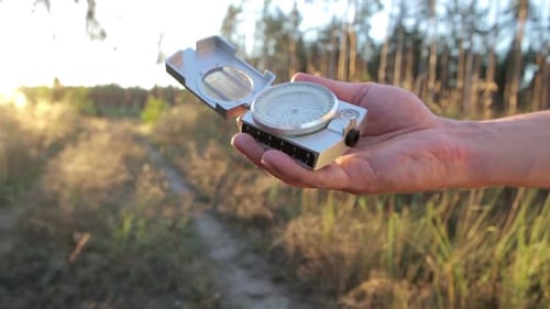 Hand Holding Compass Outdoors at Sunrise