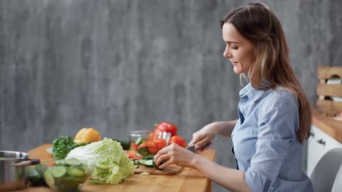 Young Woman Cuts Vegetables in Kitchen at Table