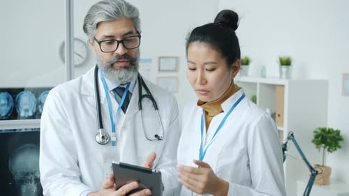 Doctors Male and Female Discussing Medical Problem Looking at Tablet Screen Standing in Office Room