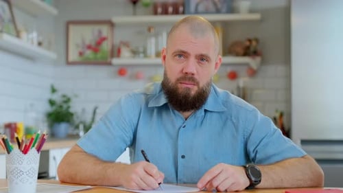 Man with Beard Writing at Table Indoors