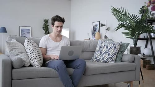 Man Using Laptop on Couch Looks Frustrated