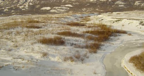 Aerial helicopter shot, lift over small river and barren trees, to reveal river valley, mountains in