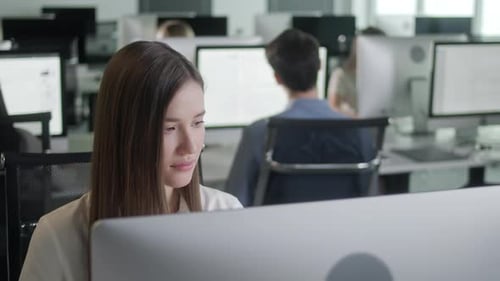 Jolie jeune femme travaillant sur un ordinateur de bureau tout en travaillant dans un grand bureau à aire ouverte