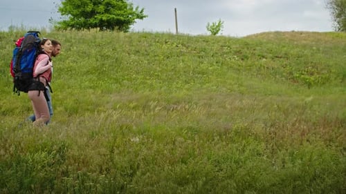 Backpackers Walking Through Grassy Rural Field