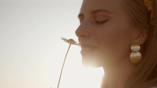 A Happy Woman is Sniffing of Chamomile on Field at Sunset