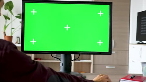 Side View of Man Sitting in Front of Computer with Big Green Screen Mock-up Chroma Typing on the