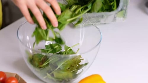 Le cuisinier verse les épinards hachés de la planche de bois à découper dans le bol en verre pour préparer le légume