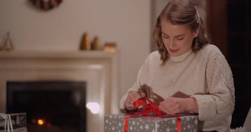 Woman Untying a Christmas Present Near Fireplace