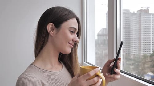 Woman Using Smartphone and Drinking Coffee at Home