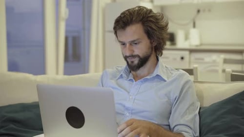 Man Uses Laptop on Couch in Living Room