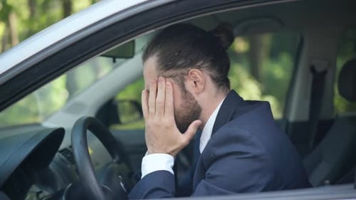 Side View Portrait of Young Stressed Caucasian Man in Suit Sitting on Driver's Seat Rubbing Temples